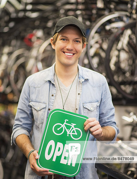 Portrait of man in bike shop holding open sign