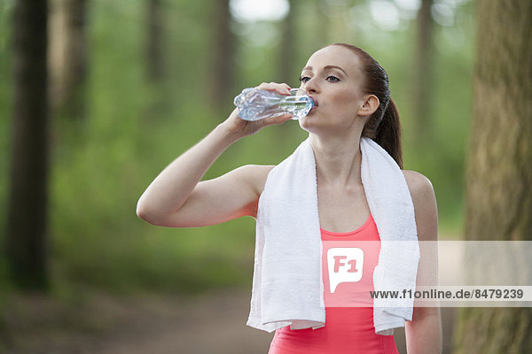 Woman drinking water during jogging in forest