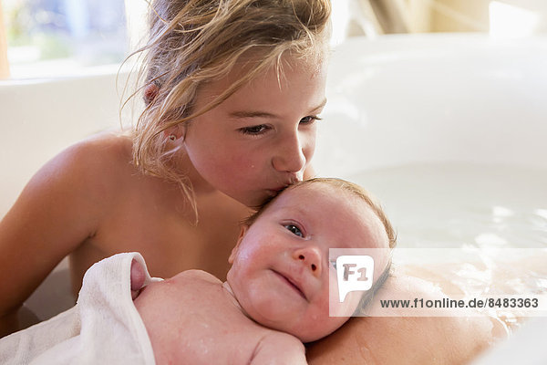 Caucasian girl kissing newborn baby in bath