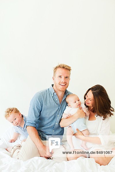 Happy parents with two sons sitting on bed