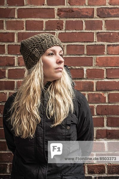 Portrait of young woman by brick wall wearing knit hat