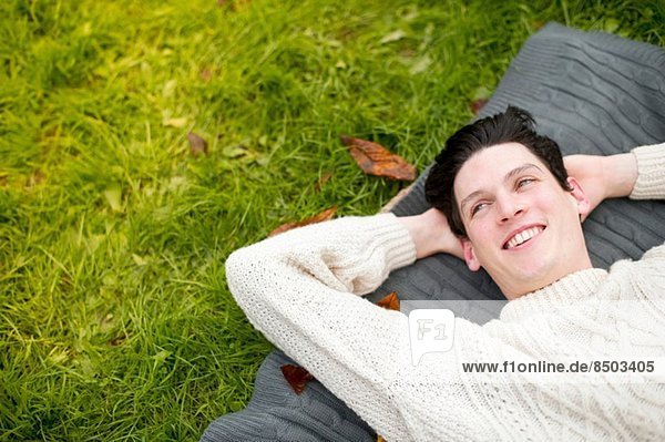 Junger Mann auf Teppich liegend mit Pullover