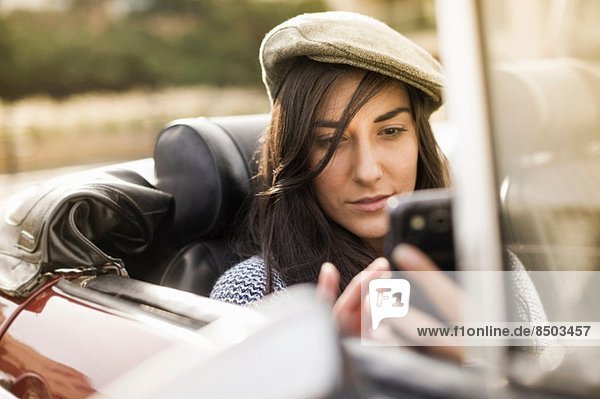 Young woman wearing flat cap in convertible using smartphone