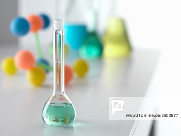 Becher mit Lösung aus chemischem Experiment mit molekularem Modell im Hintergrund auf dem Labortisch
