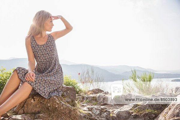Junge Frau sitzt auf Felsen und schirmt die Augen ab.