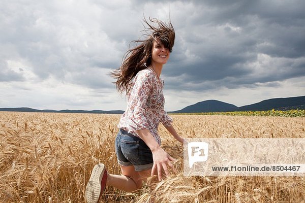 Mittlere erwachsene Frau  die durch das Weizenfeld läuft.