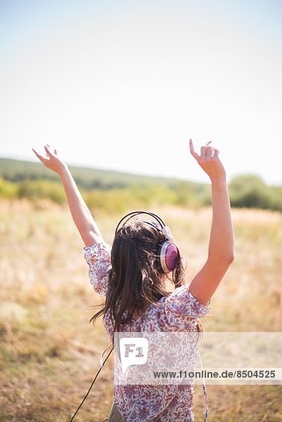 Portrait of mid adult woman dancing in field with arms raised  wearing headphones