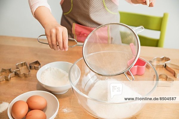 Girl sieving flour into mixing bowl