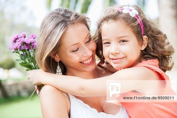 Mutter und Tochter umarmen sich und halten einen Blumenstrauss
