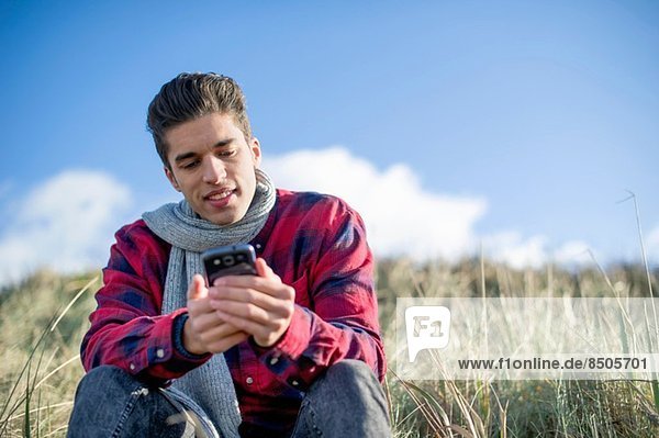 Junger Mann auf Rasen sitzend mit dem Smartphone