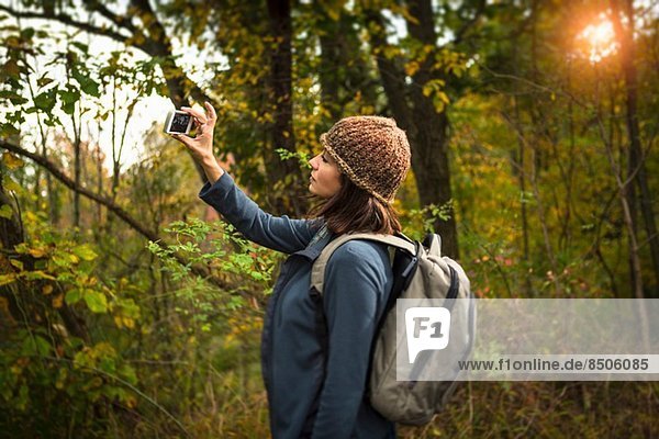 Reife Frau beim Fotografieren im Wald mit dem Smartphone