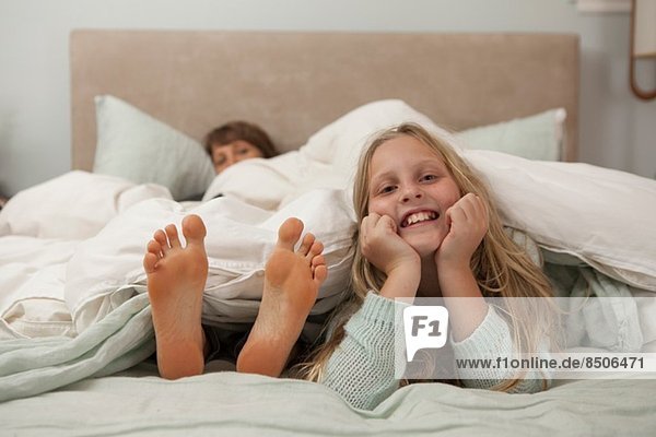 Portrait of girl lying on bed with mothers feet