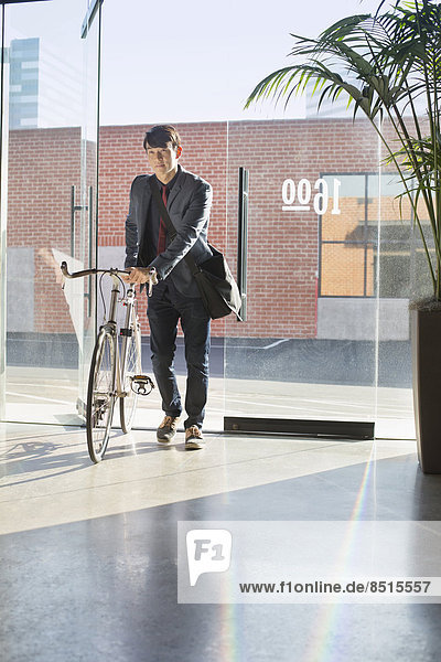 Korean businessman wheeling bicycle in office