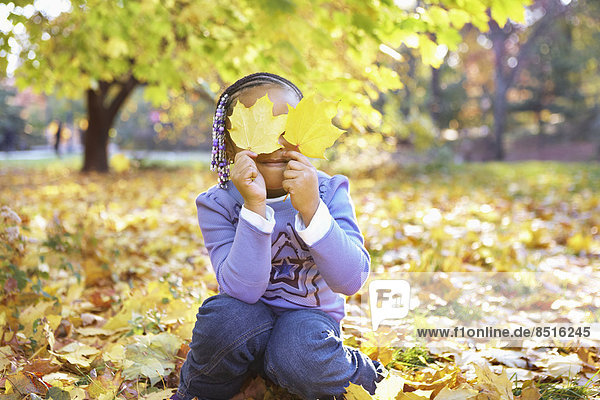 Mixed race girl holding autumn leaves over her eyes