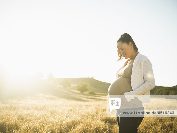 Pregnant Hispanic mother holding stomach in rural field