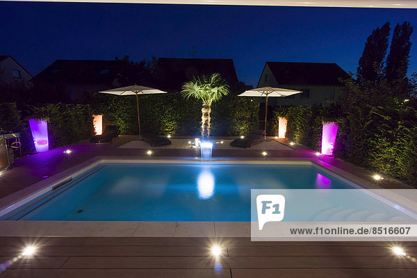 Private garden with a pool  a terrace and a palm tree  with display lighting at night  Germany