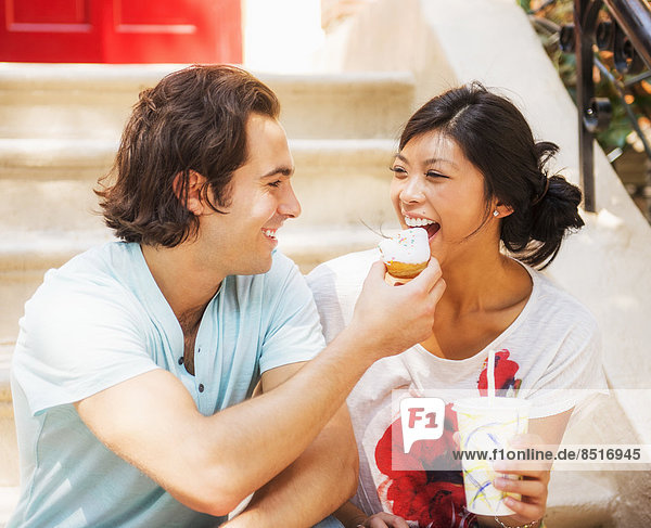 Man feeding donut to girlfriend on front stoop