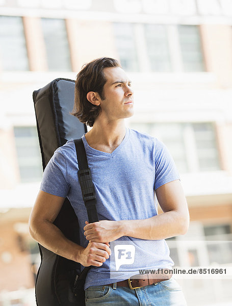 Caucasian man carrying guitar case on urban street