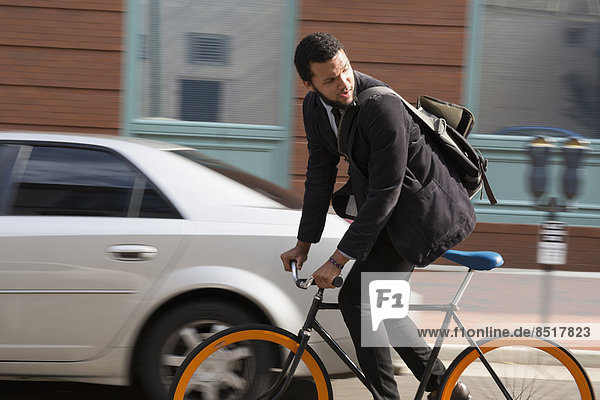 Mixed race businessman riding bicycle on city street