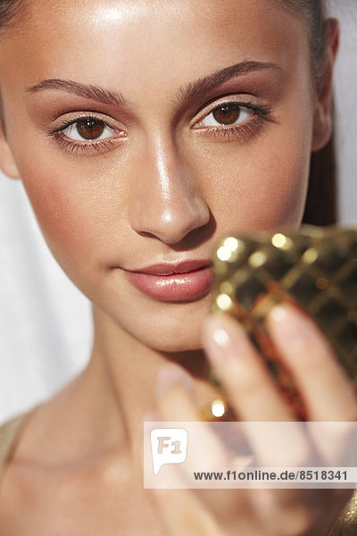 Close-up of glamorous young woman with glowing skin holding a compact mirror