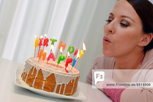 Eine junge Frau pustet die Kerzen von ihrem Geburtstagskuchen aus.