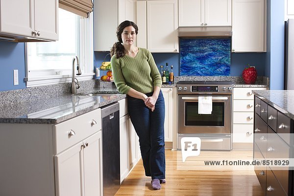 A woman relaxes in her kitchen and leans against the kitchen counter.