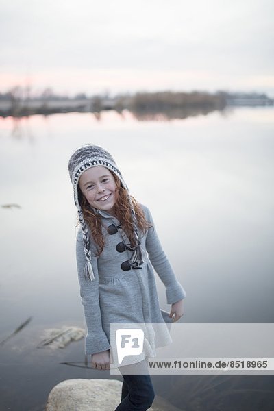 A young girl with a hat plays at the lake at dusk.