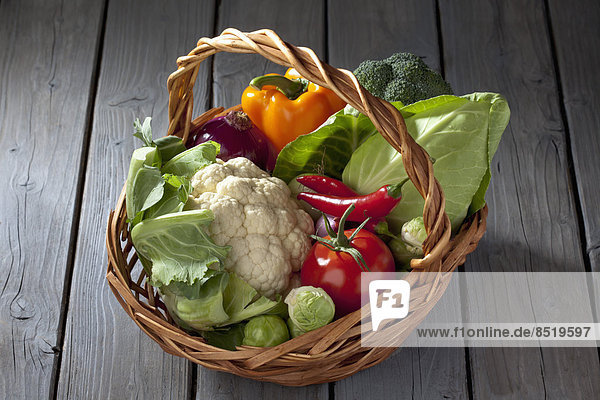 Korb mit verschiedenen Gemüsesorten auf grauem Holztisch