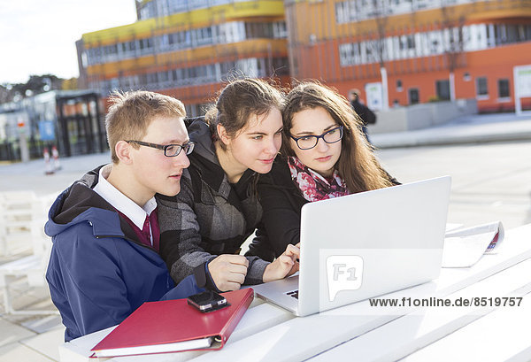 Three students using laptop outdoors