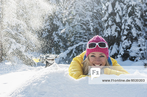 Österreich  Salzburger Land  Altenmarkt-Zauchensee  Lächelnde junge Frau im Schnee liegend  Portrait