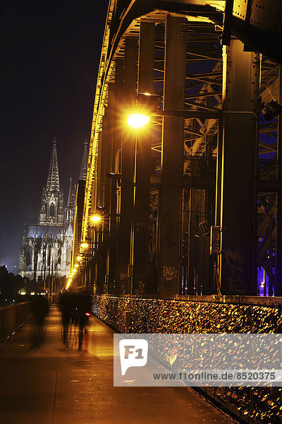 Germany  North Rhine-Westphalia  Cologne  lighted Cologne Cathedral and Hohenzollern Bridge with pedestrians at night