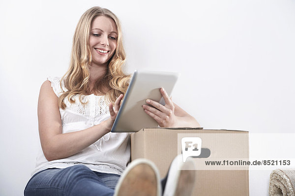 Smiling young woman with cardboard box and tablet computer