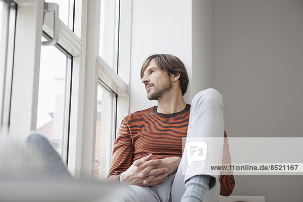 Man sitting on window sill,  looking out of window