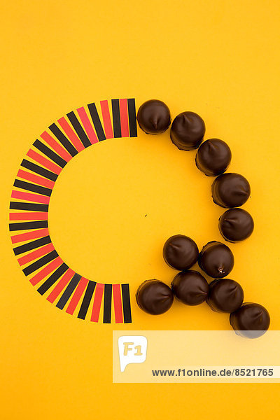 'Letter ''Q'' formed of chocolate marshmallows and red and black paper stripes at yellow background  studio shot'