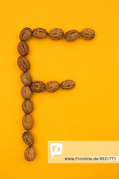 'Letter ''F'' formed of walnuts at yellow background  studio shot'