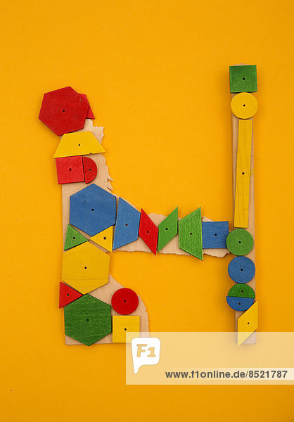 'Letter ''H'' formed of colored geometric wooden forms at yellow background  studio shot'