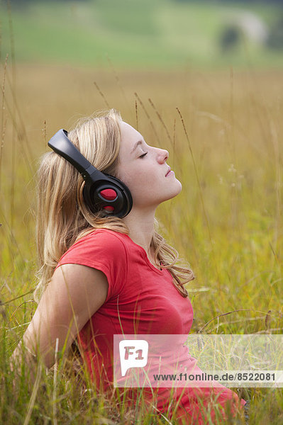 Österreich  Salzkammergut  Mondsee  junge Frau mit Kopfhörer auf einer Wiese sitzend