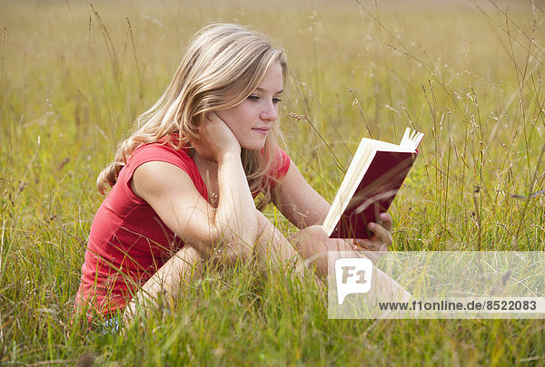 Austria  Salzkammergut  Mondsee  young woman reading book in a meadow
