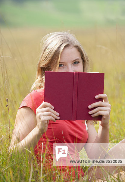 Österreich  Salzkammergut  Mondsee  junge Frau mit Buch auf einer Wiese sitzend