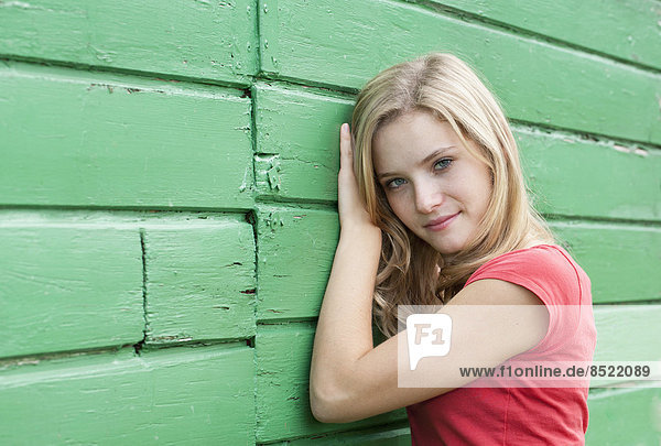 Österreich  Salzkammergut  Mondsee  Portrait einer jungen Frau  die sich an eine grüne Holzfassade lehnt