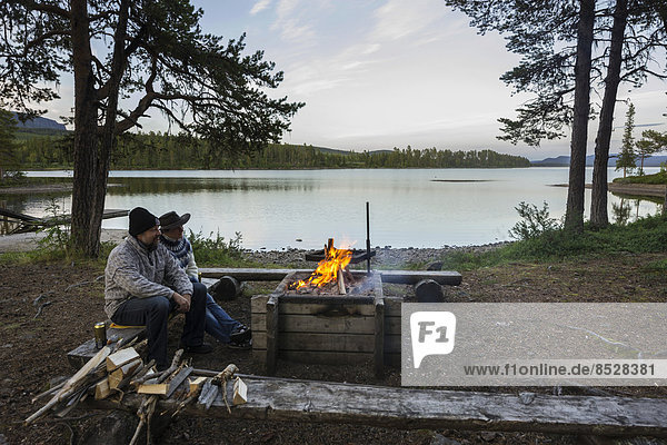 Paar sitzt vor Lagerfeuer auf dem Campingplatz der Insel Årrenjarka  Kvikkjokk  Norrbottens län  Schweden