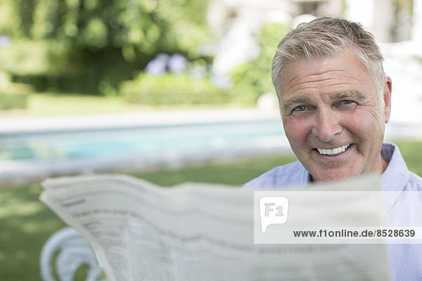 Älterer Mann beim Zeitungslesen am Pool