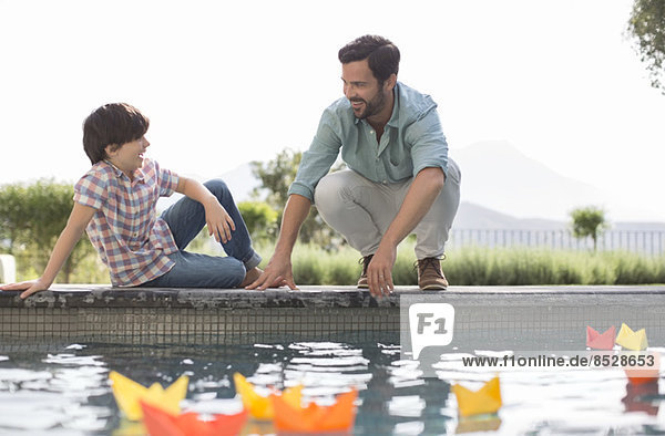 Vater und Sohn beobachten Origami-Boote im Schwimmbad
