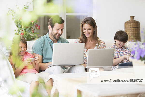 Familie mit Laptops,  digitalem Tablett und Handy auf Terrassensofa
