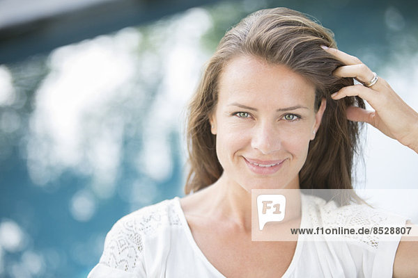 Frau lächelt mit der Hand in den Haaren am Beckenrand