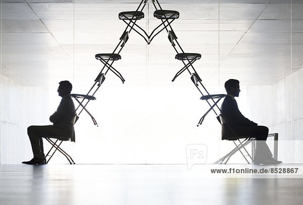 Geschäftsleute sitzen an gegenüberliegenden Enden des Bürostuhls Installationskunst