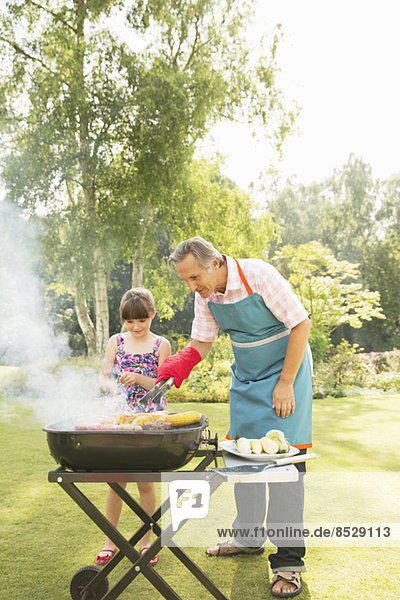 Grandfather and granddaughter grilling at barbecue in backyard