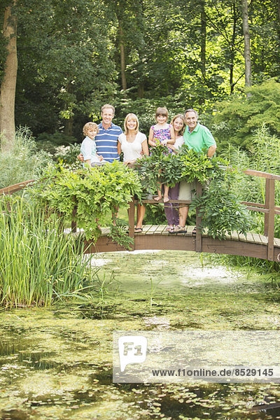 Multi-generation family standing on wooden footbridge over pond