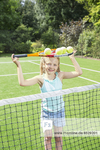 Mädchen mit Tennisschläger und Bällen auf Rasenplatz