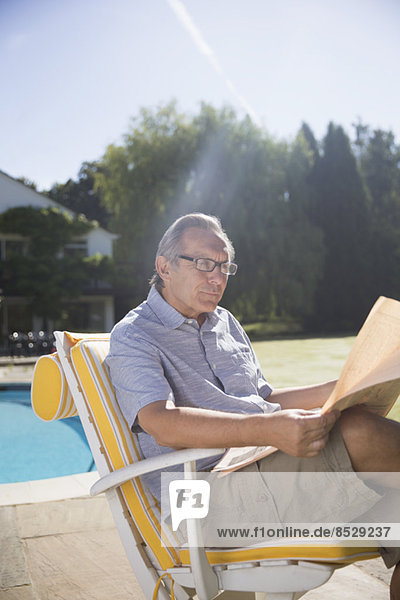 Man reading newspaper at poolside